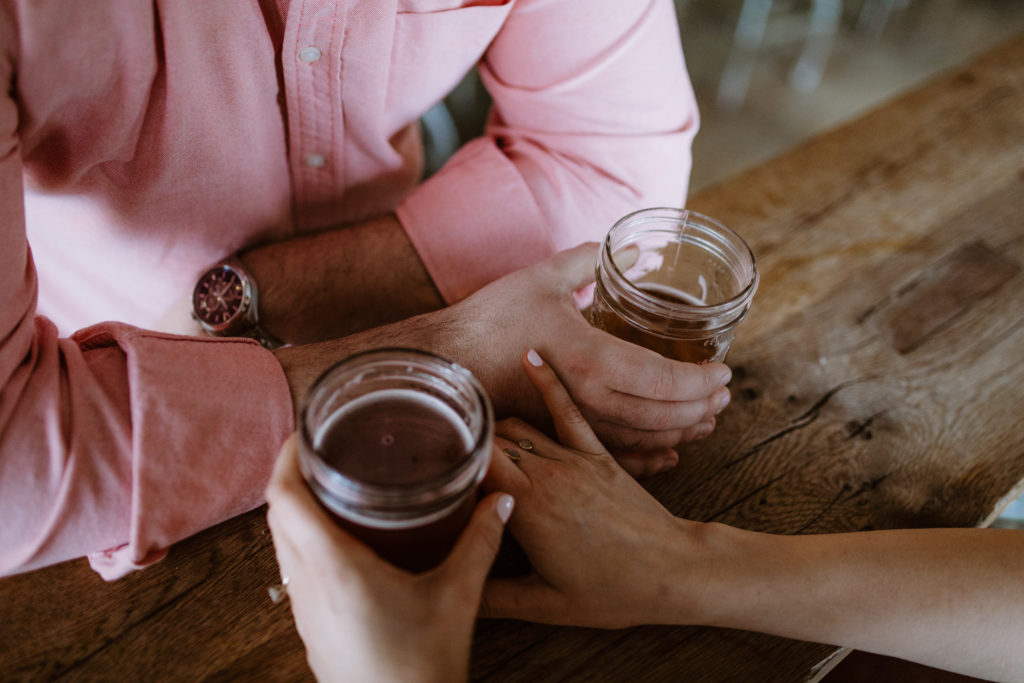 a man and woman's hands while holding jars of beer