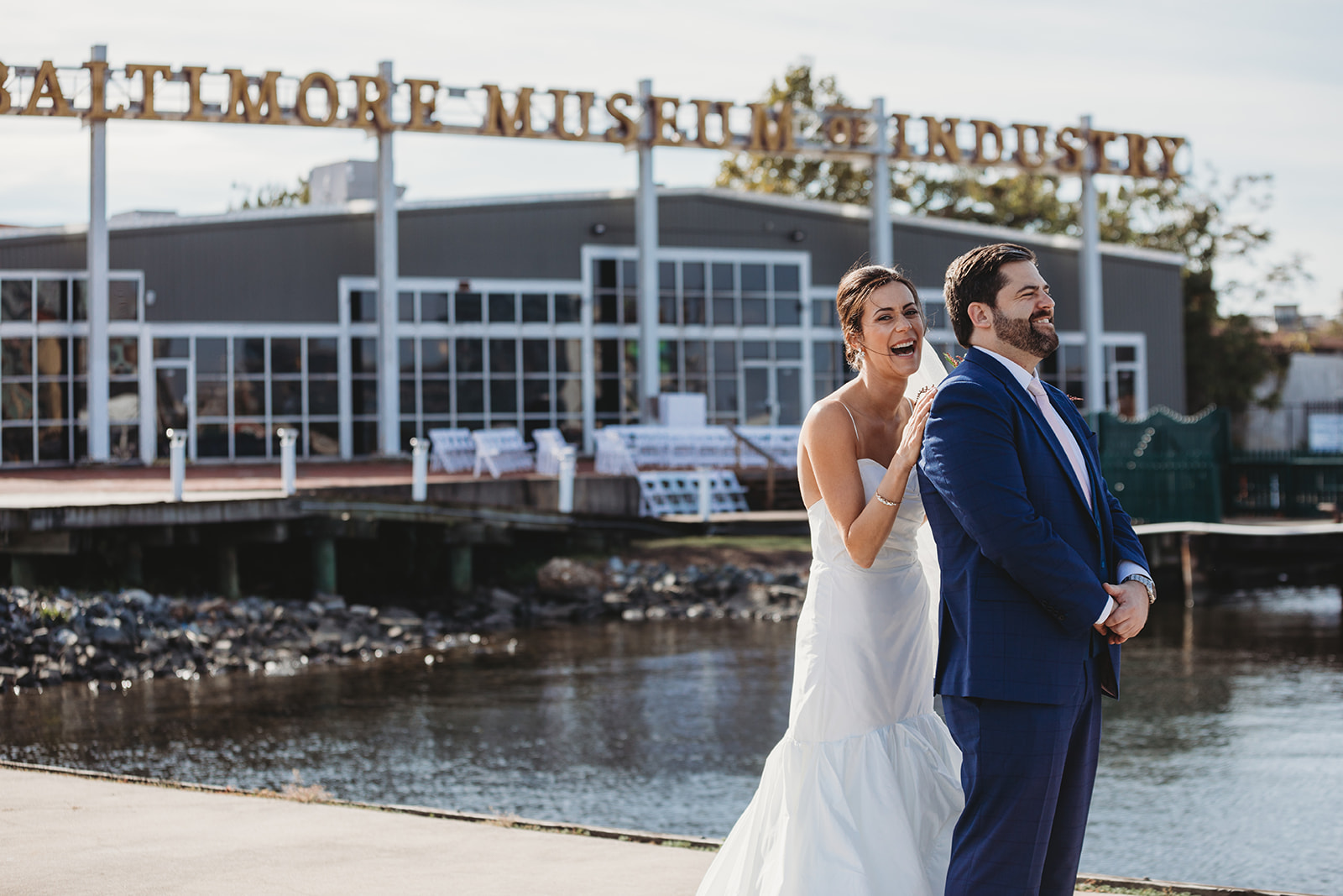 a bride and groom stand laughing in front of the Baltimore museum of industry