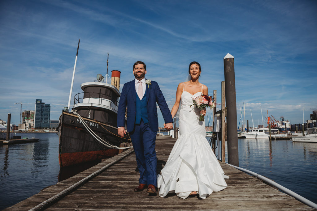 a bride and groom walk on the pier in front of the baltimore museum of industry