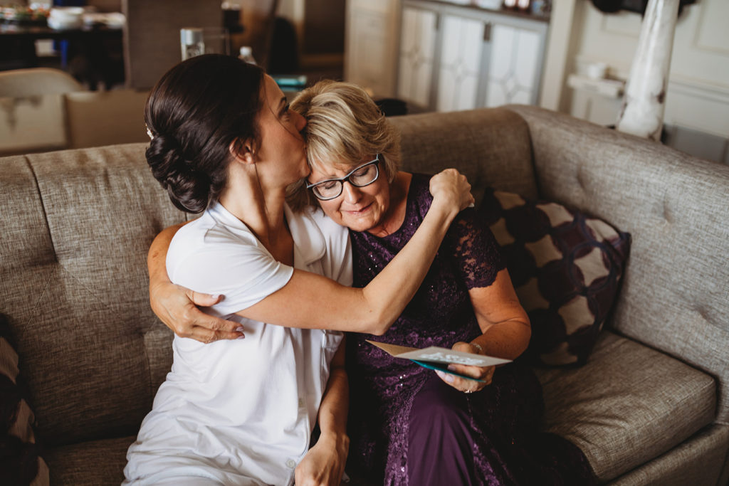 a bride kissing her mother on the head in a hotel room