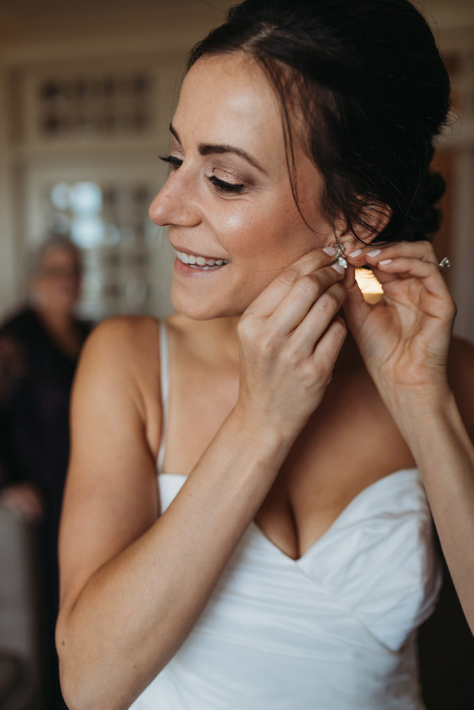 a bride puts on her earring and smiles
